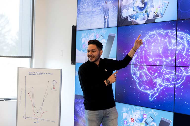 A male student smiles as he shows the digital image of a brain on the wall. 