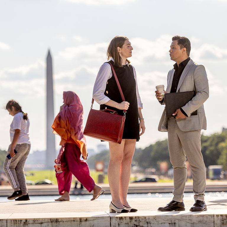 a male and female dressed in business attire have a conversation with the national mall and Washington monument in the background