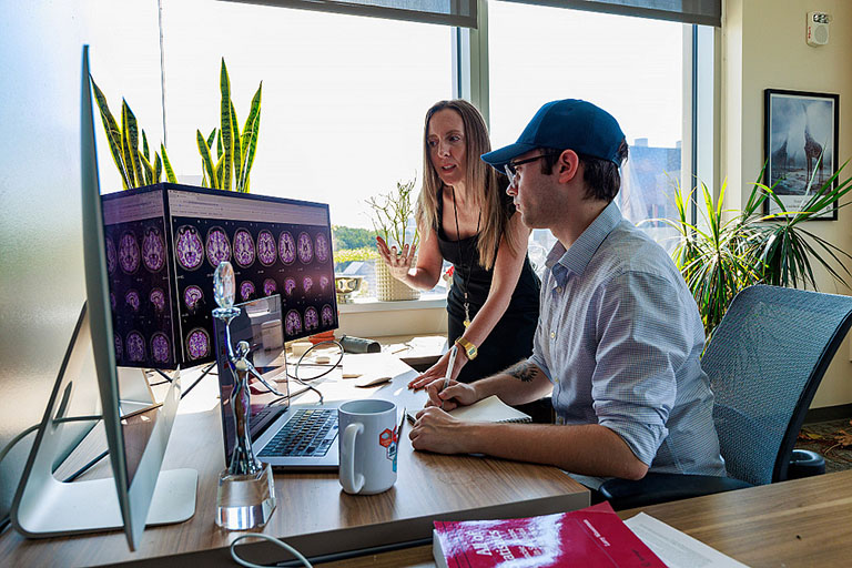 IU researcher Amanda Mejia and a grad student look at brain MRI images on a computer screen.