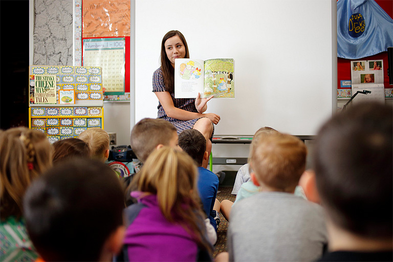 An Indiana teacher is reading a story book aloud to their young students. 