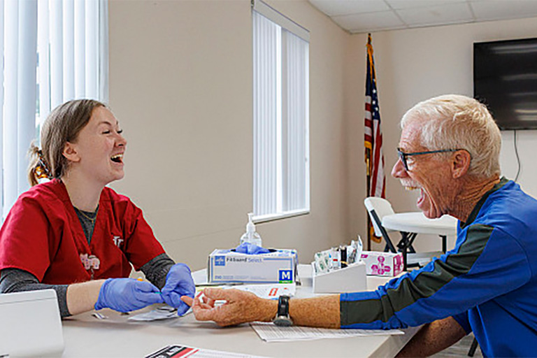 A man laughs as he speaks with a nurse who is preparing to test his cholesterol levels.