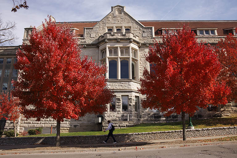 A student walks past two trees with bright red leaves outside Franklin Hall.