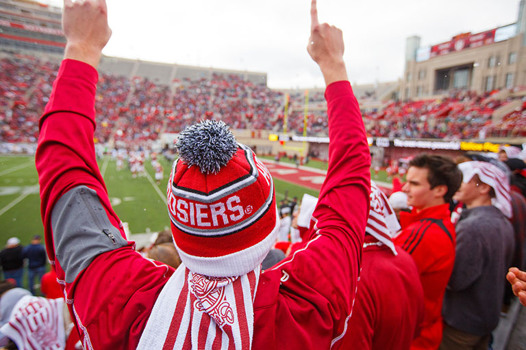 A student wearing a red and white knit cap gives a "We're number one" hand sign at a game.