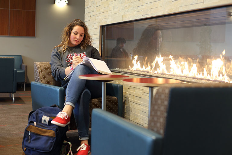 A young woman studies next to a fireplace.