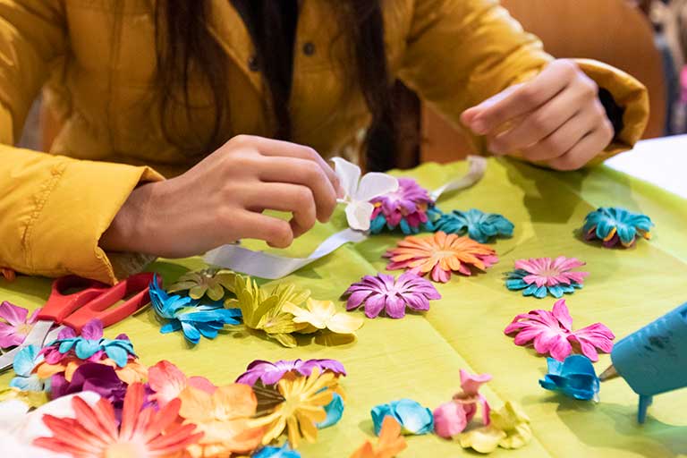 A student works with colorful faux flowers and a glue gun.