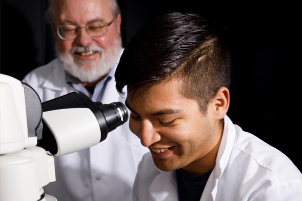 An Indiana University student uses a microscope while a professor looks on.