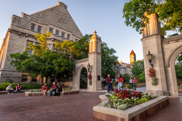 Students stand by the large, limestone Sample Gates on the Indiana University Bloomington campus.